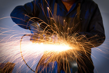 Factory worker makes sparks using electric grinder isolated.