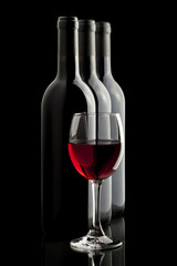 Elegant red wine glass and a wine bottles in black background