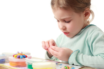 Side view of little girl sitting at table and carefully sculpts