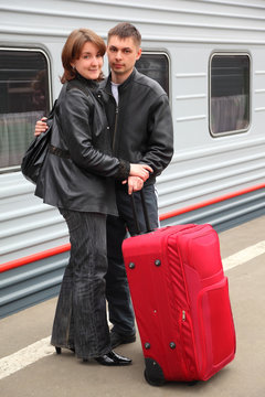 husband and wife with big red bag stand on perron near train
