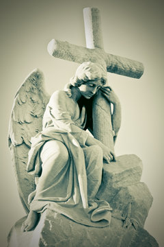 Grunge image of a sad angel holding a cross in greenish shades