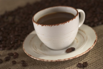 Hot fresh coffee in cup surrounded by coffee beans