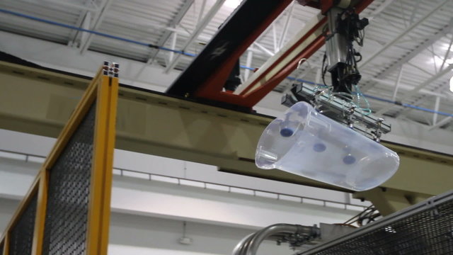 A robotic arm grabs a plastic trash can and places it on the conveyor belt.
