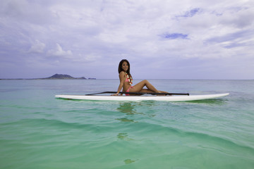 asian woman in pink bikini on a paddle board in hawaii