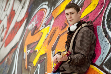 Style teen boy with guitar at graffiti background.