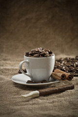 cup with coffee beans and cinnamon on burlap