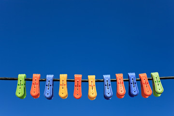 Line of multicolor plastic clothes pegs hanging in front blue sk