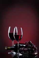 Wine in glasses with grape and bottle on red