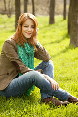 Obraz premium Beautiful red-haired girl sitting at green grass at park.