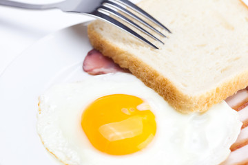 bacon with  fried  eggs on a plate, fork and bread isolated on w