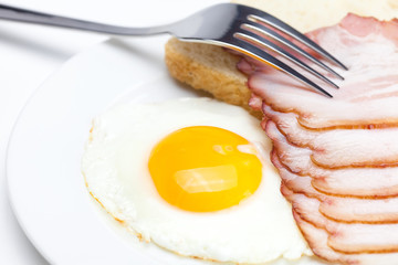 bacon with  fried  eggs on a plate, fork and bread isolated on w