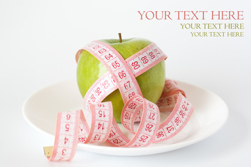 Green apple and measuring tape on a white plate