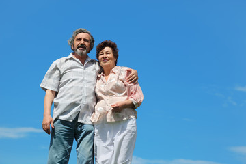 old man and woman standing and embracing, blue sky