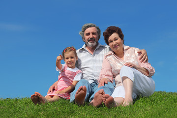 Fototapeta premium old man and woman sitting on lawn with their granddaughter