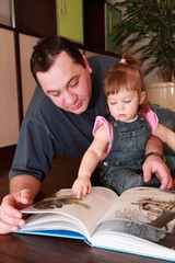 father and little daughter in denim jumpsuit reads book