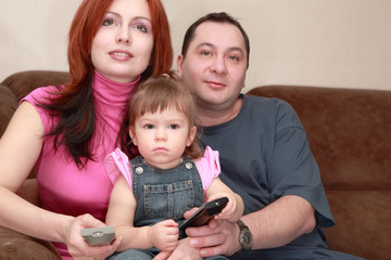 mother, father and daughter sitting on couch and watch TV