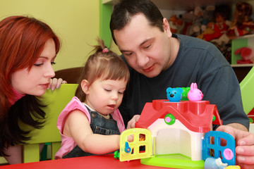 mother and father playing with daughter, toy house