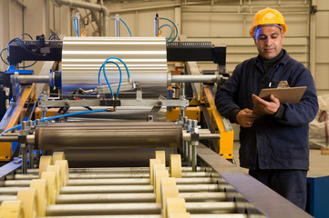 Factory worker processing roll of steel sheet.