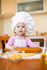 Little girl makes dough on kitchen with rolling pin