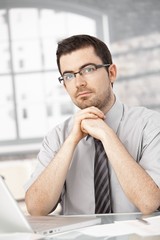 Naklejka premium Portrait of young man sitting at desk using laptop