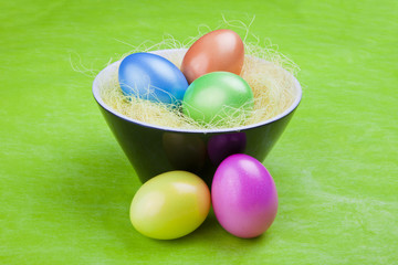 Colorful Easter eggs in a bowl, on a green background