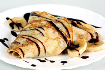 close-up crepe with bananas and chocolate on white plate