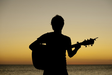 silhouette of ten boy playing guitar against sunset sky