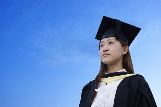 Serious female asian graduate with sky background