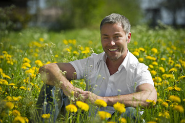 Mann sitzt in einer Blumenwiese und lacht.