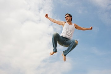 Fototapeta na wymiar Happy young man jumping against blue sky