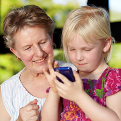 Grandmother and her cute granddaughter playing with cellphone