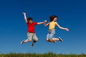 Girl and boy jumping, running against blue sky