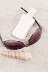 Fototapeta na wymiar Sun Block with Sunglasses and Shell on the Sand