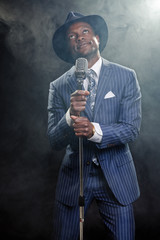 Black man with blue striped suit and blue hat singing.