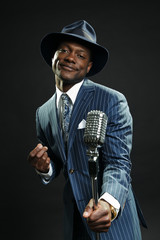 Black man with blue striped suit and blue hat singing.