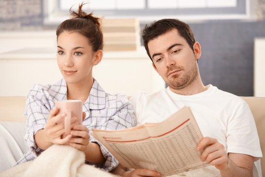 Young couple in bed man reading woman drinking tea
