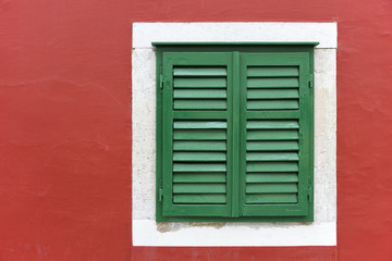 Fototapeta premium Single window with green shutters set in red wall in Skradin