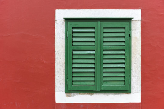Single window with green shutters set in red wall in Skradin