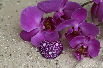 Herz und Orchideenblüte im Sand