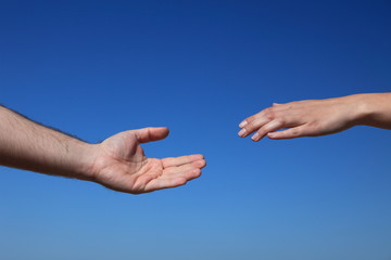 Zwei Personen reichen sich die Hände vor blauem Himmel