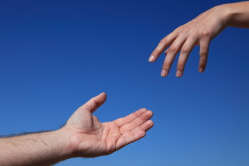 Zwei Personen reichen sich die Hand vor blauem Himmel