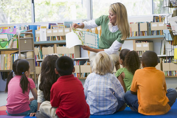 Kindergarten teacher reading to children in library - obrazy, fototapety, plakaty