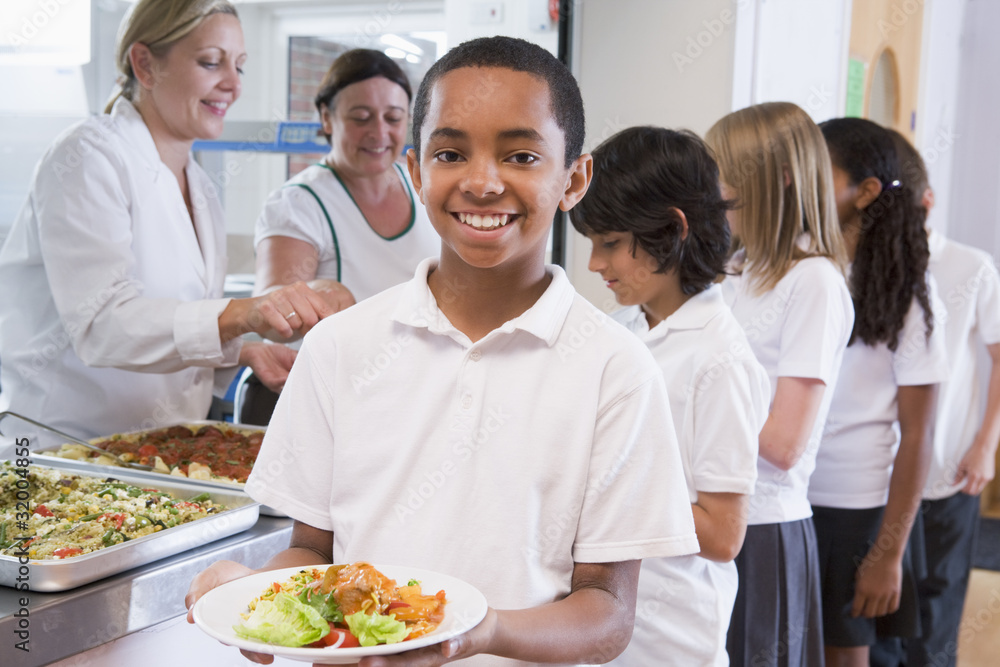 Wall mural Schoolboy holding plate of lunch in school cafeteria