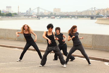 Four girls in same black clothes dancing on embankment