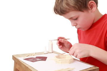 little boy in T-shirt crafts at small table, glue, side view