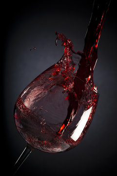 Red wine pouring down into wine glass on black background