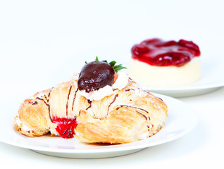 Creme filled croissant and strawberry cheesecake on a white back