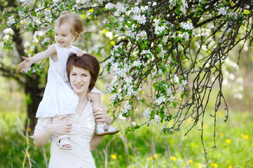 Young mother and her daughter in blossoming apple trees