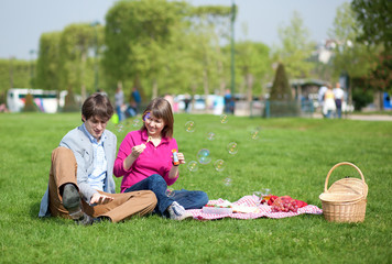 Happy young couple having a picnic and making bubbles