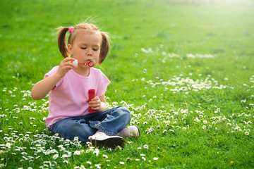 Fototapeta premium Little girl is sitting on green meadow